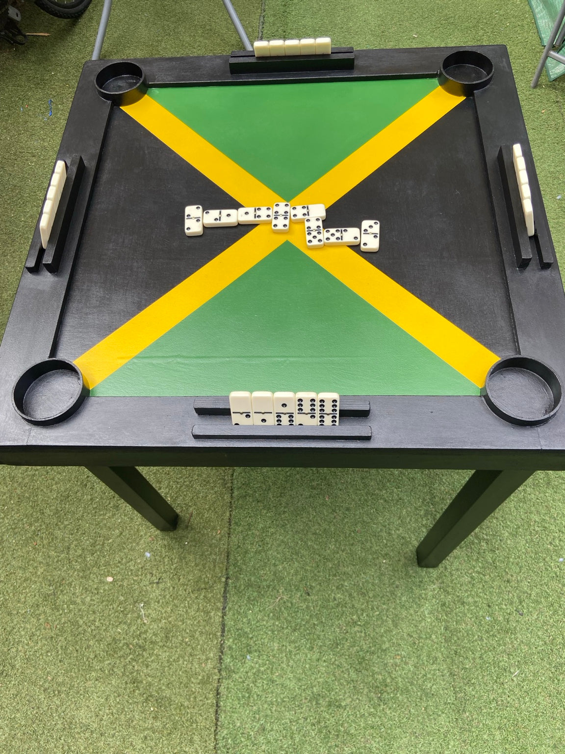 Handmade Jamaican flag domino table showing its legs, four cup holders and domino holders. Dominoes shown are not included.